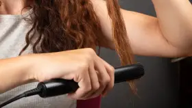 Dłoń prostuje brązowe włosy prostownicą.