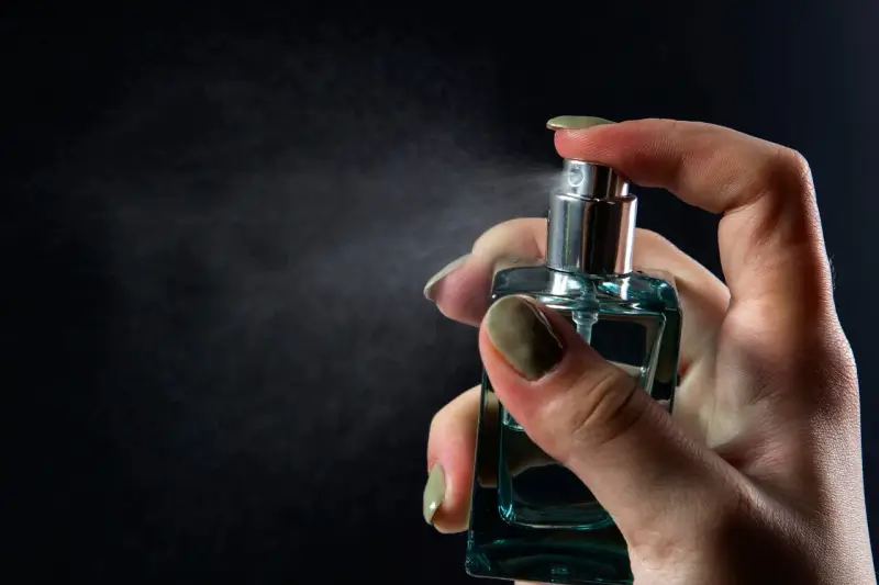 Dłoń trzymająca buteleczkę perfum i rozpylająca mgiełkę.